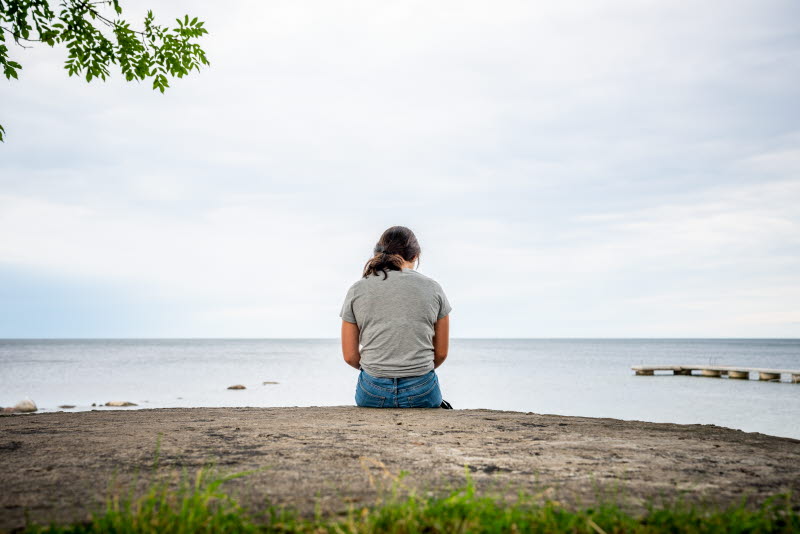 En kvinna sitter ensam vid en strandkant.