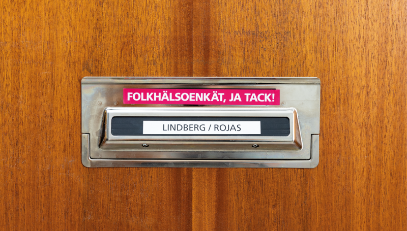 Ett brevinkast på en trädörr, med namnen Linberg/Rojas och en klisterlapp där det står Folkhälsoenkät, ja tack